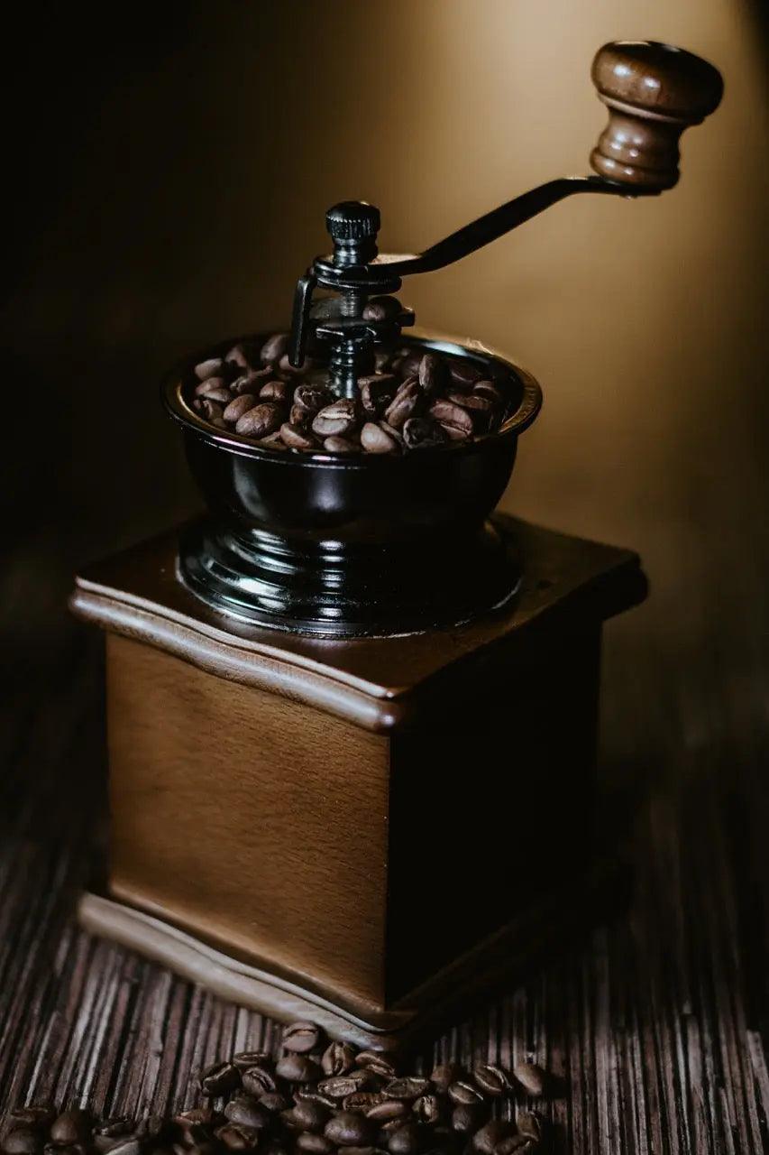 manual coffee grinder with beans and hand crank on wooden surface for grinding coffee beans